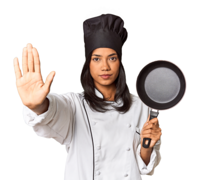 Young Filipina chef holding pan by handle standing with outstretched hand showing stop sign, preventing you.