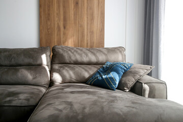 Grey comfortable sofa with blue cushion next to the big sunny window in the living room, modern living and home decor concept.