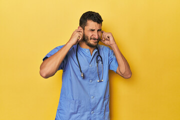 Young Hispanic male nurse Young Hispanic male nurse poses confidently covering ears with hands.< mixto >