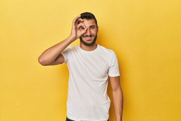 Fototapeta na wymiar Young Hispanic man on yellow background excited keeping ok gesture on eye.