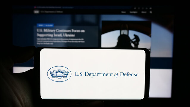 Stuttgart, Germany - 10-29-2023: Person holding cellphone with logo of United States Department of Defense (DoD) in front of webpage. Focus on phone display.