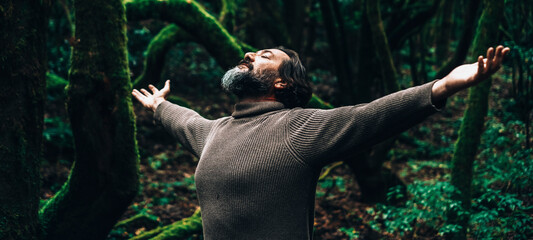 Portrait of overjoyed man outstretching arms in outdoors leisure activity with dark beautiful green forest in background. People and nature love. Environment and woods protection concept lifestyle - obrazy, fototapety, plakaty