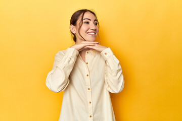 keeps hands under chin, is looking happily aside.