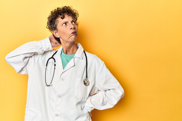Caucasian mid-age female doctor on yellow studio touching back of head, thinking and making a...