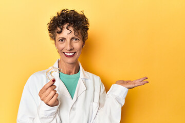 Doctor with invisible dental aligner on yellow showing a copy space on a palm and holding another...