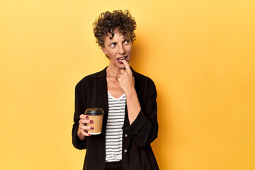 Businesswoman holding takeaway coffee on yellow relaxed thinking about something looking at a copy space.