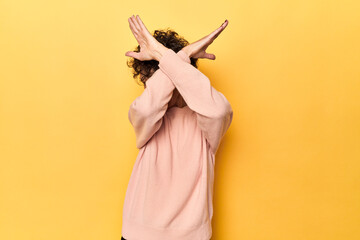 Mid-aged caucasian woman on vibrant yellow keeping two arms crossed, denial concept.