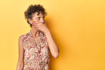 Mid-aged caucasian woman on vibrant yellow thoughtful looking to a copy space covering mouth with hand.