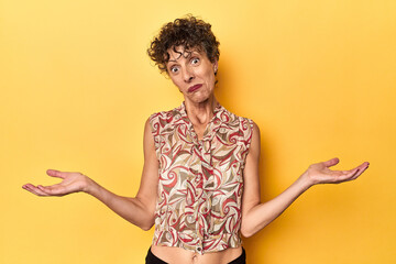 Mid-aged caucasian woman on vibrant yellow doubting and shrugging shoulders in questioning gesture.