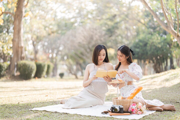 Two beautiful LGBT young women in casual clothes and summer hats Carefree woman having a picnic outside Positive model sitting on the grass eat fruit and cheese Take a selfie. LGBT concept