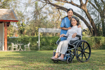 Young female in uniform with senior patient in a wheelchair chilling out in park