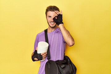 Man with protein jar and backpack on yellow excited keeping ok gesture on eye.