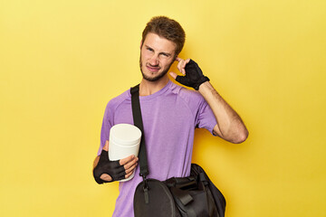 Man with protein jar and backpack on yellow covering ears with hands.