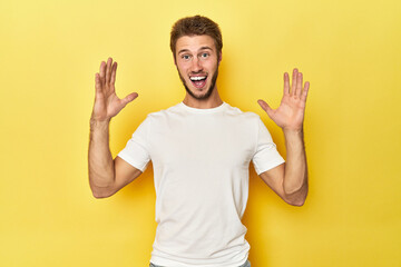 Young Caucasian man on a yellow studio background celebrating a victory or success, he is surprised...