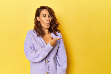 Middle-aged woman on a yellow backdrop pointing to the side