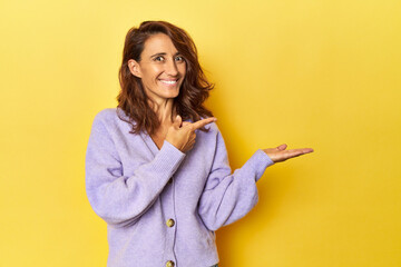 Middle-aged woman on a yellow backdrop excited holding a copy space on palm.
