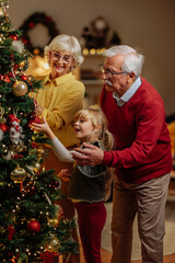 Grandparents helping granddaughter decorate christmas tree