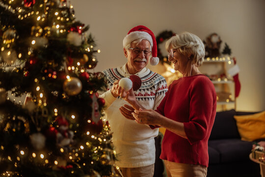 Elderly couple holding bulbs while decorating a Christmas tree