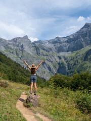 Vertical rear view photo of a girl celebrating during a hiking route with stunning views of mountains and forests - concept of hiking, well-being, and healthy living