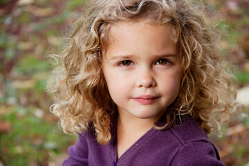 portrait of a pretty young female child with blonde curly hair and brown eyes looking at the camera with an autumnal background 