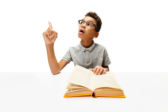 African-American boy, pupil sitting with opened book, create new idea during doing homework. Child study and learn for preschool. Online education. Concept of childhood, International Knowledge Day. - Powered by Adobe