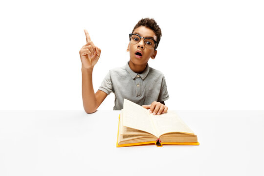 Surprise African-American boy sitting with opened book, create new idea during doing homework. Child study and learn for preschool. Online education. Concept of childhood, International Knowledge Day.