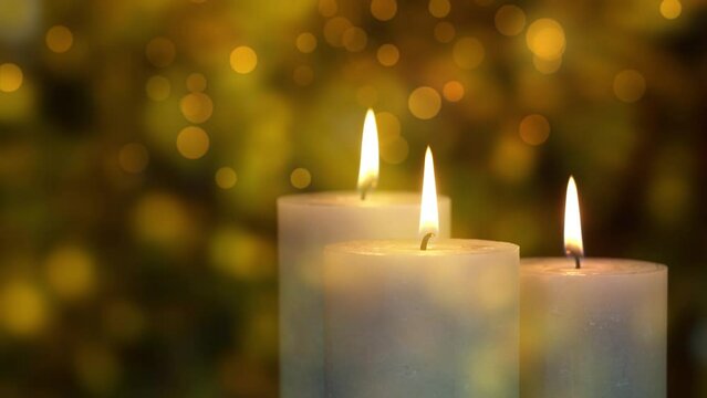 three white slowly rotating candles in front of a glowing golden bokeh light animation background, festive merry christmas or happy new year holiday decoration backdrop closeup