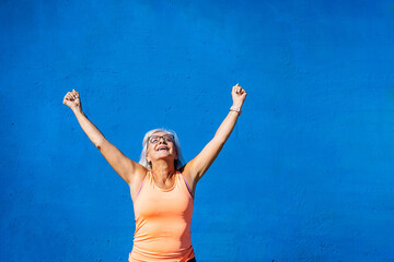 Sportive elder woman feeling free raising arms and fists