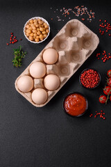 Raw chicken eggs in a box, cherry tomatoes, chickpeas, spices, salt and herbs