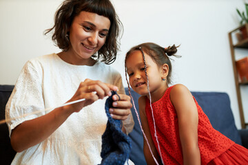 Low angle portrait of happy smiling female enjoying knitting while her little daughter watching her...