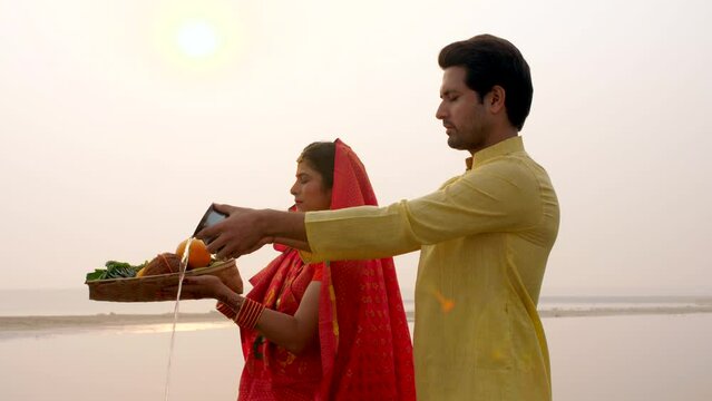 Traditionally dressed Indian couple worshiping God Sun - a celebration of Chhath Pooja festival  Bihari family  offering water. A man and a woman offering prasad to the Lord Sun on the occasion of ...