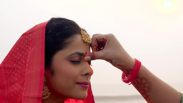 Closeup shot of a woman on Chhath Pooja performing the ritual of the festival   Puja in Bihar  Jharkhand  Nepal  West bengal  Sun prayer. Applying Sindoor to a woman in the traditional outfit of Ch...