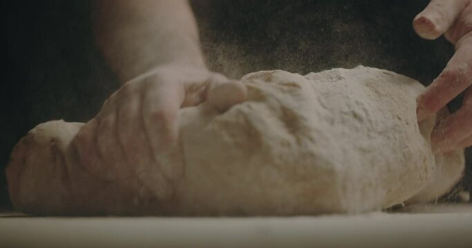 Flour falling on dough and man kneading on counter
