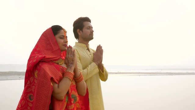 Indian Hindu female and her husband performing rituals of chhath puja while standing in river to worship lord sun. An Indian couple praying to sun on the occasion of chhath puja - Bihari festival  ...