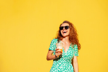 Joyful young curly hair woman in sunglasses holding glass of juice in hand and laughing.