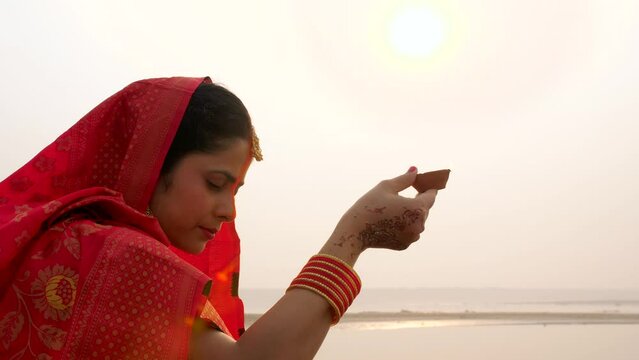 Indian woman holding an earthen lamp in her hand - faith of God  red saree  offering prayers to sun. Hindu woman with handmade clay lamp - Chhath Puja  Bihari festival  Hindu festival  newly wed wo...