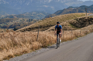 Man cyclist training in the mountains a gravel bike with a beautiful view. Cycling holiday in Romania. Сyclist wearing cycling kit and helmet. Sportsman riding in the beautiful natural surroundings.