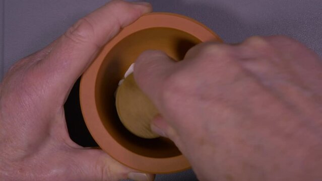 Closeup overhead shot of hands using an earthenware or clay mortar bowl and a wooden pestle, to grind and crush some plain white tablets into a powder. 