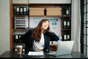 Asian woman feeling migraine head strain.Overworked businesswoman financier while working on laptop and tablet at office..