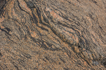 Granite surface in brown color. Stone structure with wavy curved lines diagonally and a small line...