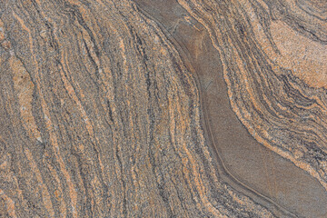 Fototapeta premium Wavy pattern from a brown granite stone. Background pattern natural stone with broken lines. Surface with dark color interruptions. Diagonally meandering line structure