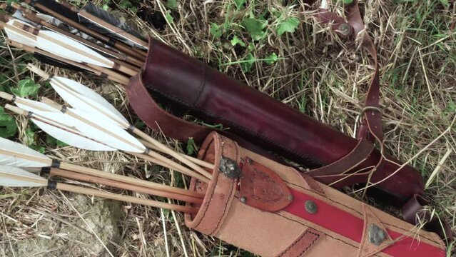 close-up overview of two ancient Etruscan leather quivers laid on the grass with several arrows inserted with white fins