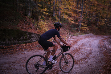 Fototapeta premium Fit male cyclist riding a gravel bike in autumn forest. Amazing autumn foliage. Cyclist training on beautiful autumn forest trail. Sport motivation. Adventure travel on bike. 