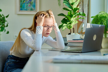 Sad pensive young teenage girl sitting near smartphone laptop at home.
