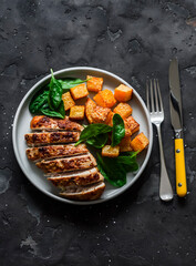 Roasted chicken breast, pumpkin and spinach - a delicious healthy lunch on a dark background, top view