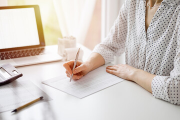 Woman accountant using a calculator and laptop computer while counting taxes at the white table in...