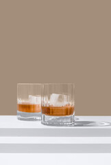 Dos vasos de whisky con hielo sobre un fondo marrón	