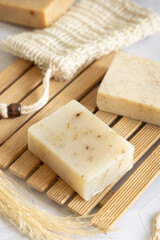 Beige handmade soap bar on wooden tray near soap saver bag  close up