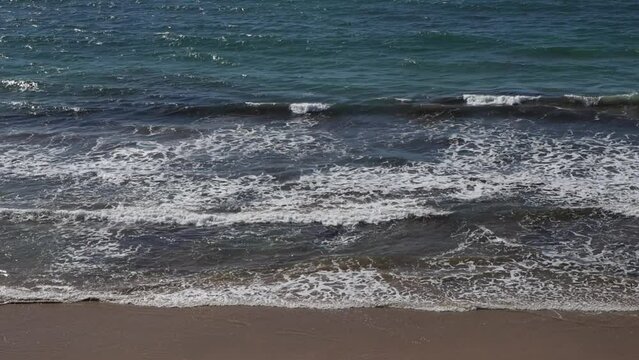 Ondas do mar rebentando calmamente na areia da praia. Mar calmo com ondas pequenas. Oceano azul numa praia deserta.