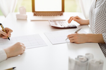 Two accountants using a calculator and laptop computer for counting taxes or revenue balance while...